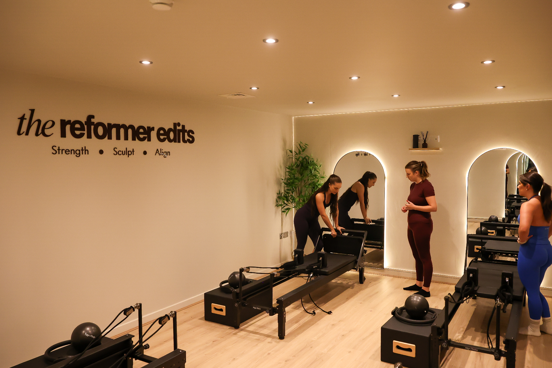 The Reformer Edits studio wall — cream walls with the wordmark above four Align-Pilates reformers